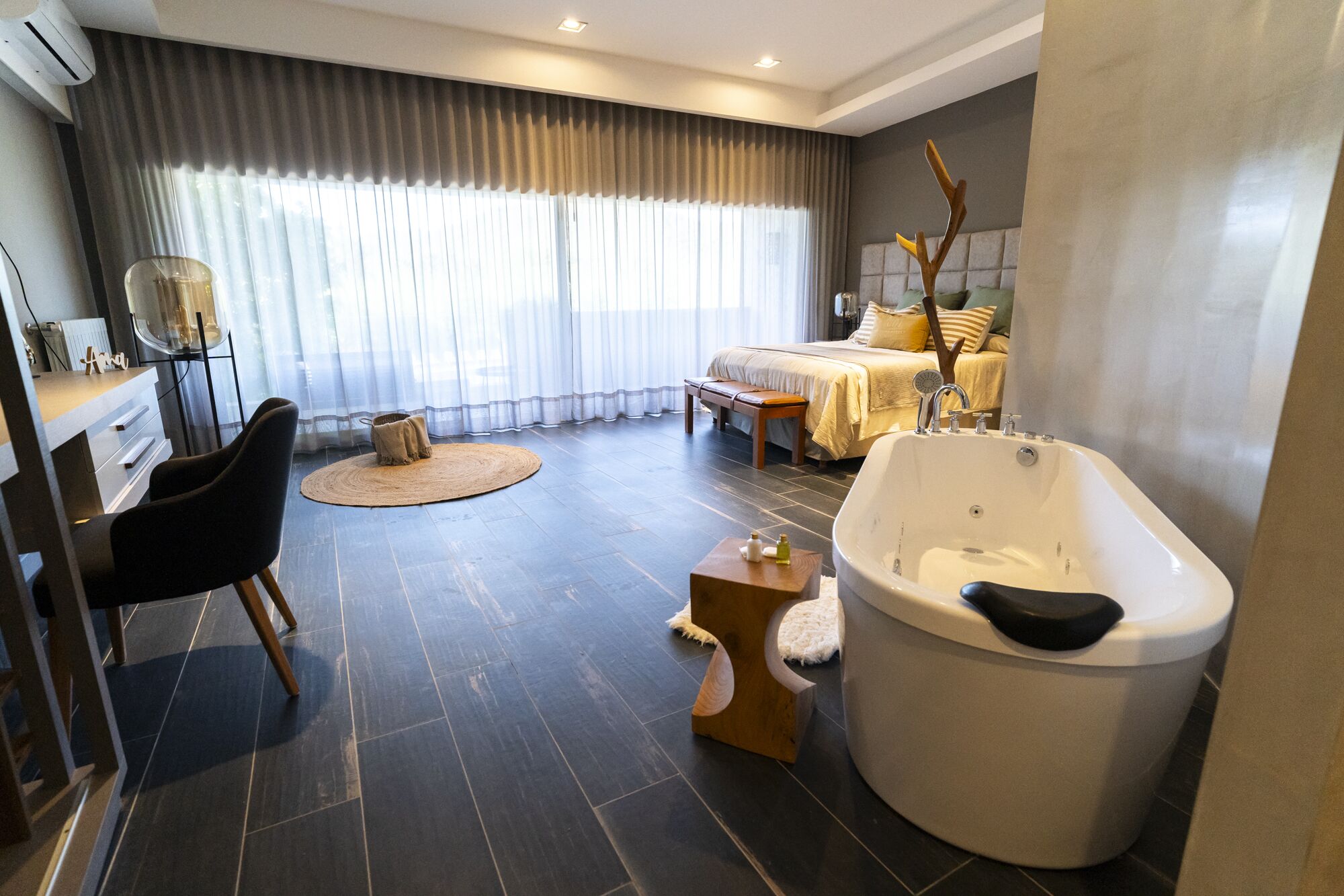 Un baño moderno con una bañera independiente, un tocador con espejo y una zona de estar con una silla y una alfombra redonda pequeña.
