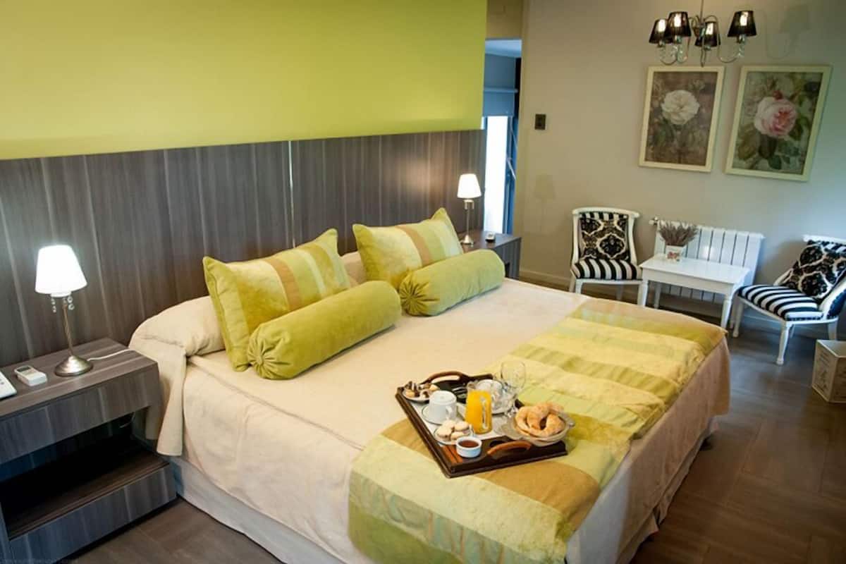 A hotel room with a bed, a bedside table with a lamp, a tray with breakfast items, and a chair with a striped cushion.