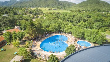 Una gran piscina al aire libre rodeada de árboles y un pequeño edificio, con vista a un paisaje montañoso al fondo.