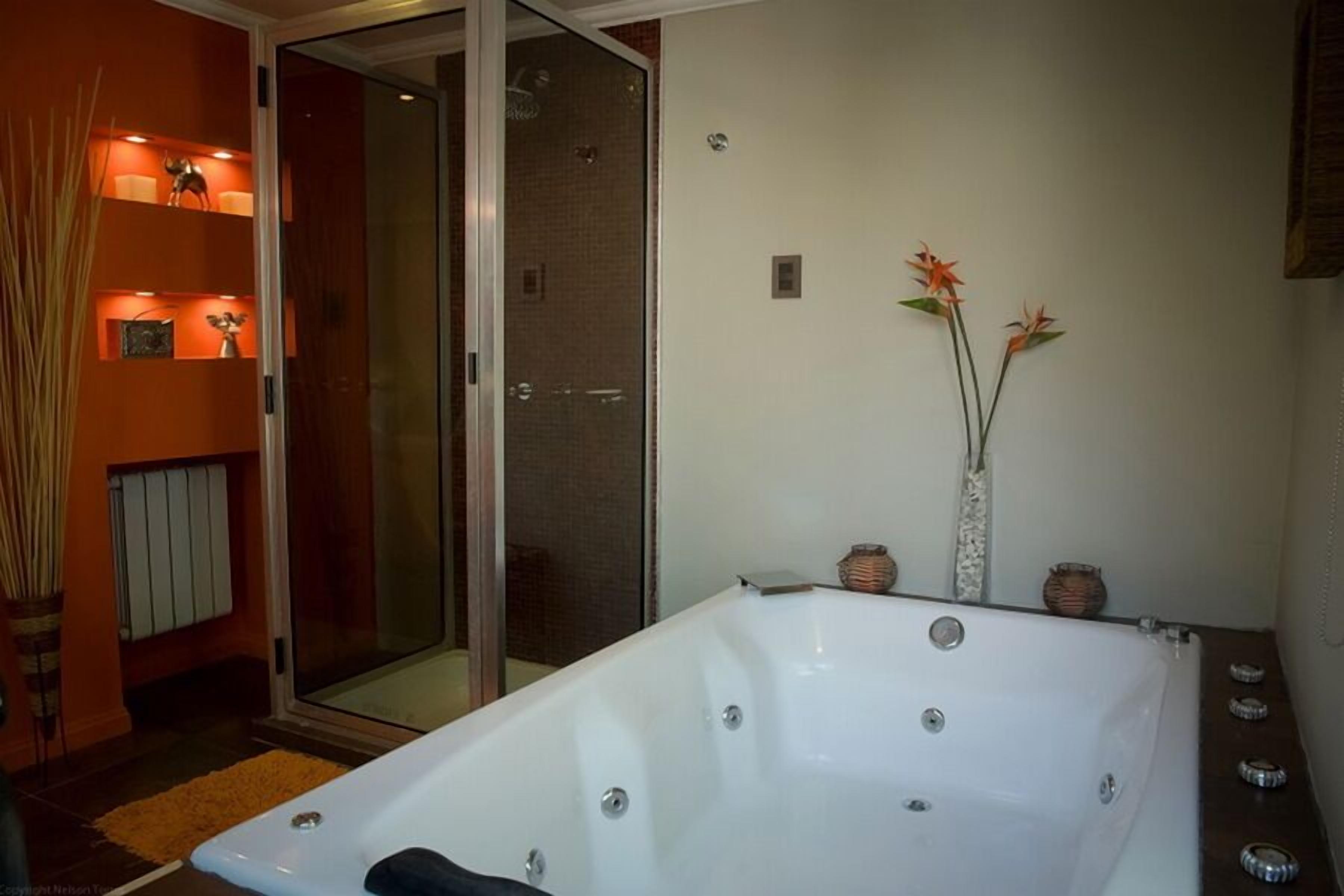 A modern bathroom with a large bathtub, a glass shower enclosure, and decorative vases on the wall.