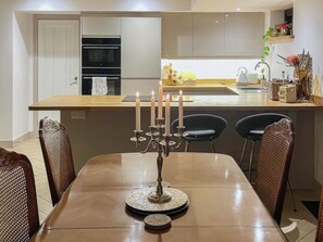A modern kitchen with a dining area, featuring a central island with a candelabra, a built-in oven, and a sink.