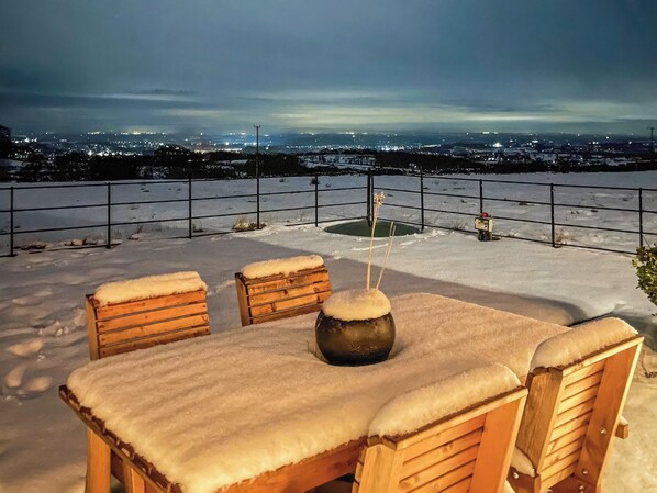 A snow-covered outdoor seating area with a view of a cityscape at night.