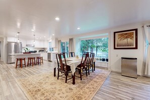 A modern kitchen with a dining area, large windows, and a refrigerator.