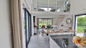 A modern, open-plan living space with a dining area, a kitchen, and a large glass door leading to a garden. - Les Herbes Folles - Tregastel (TREGASTEL)