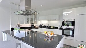 A modern kitchen with a central island, stainless steel appliances, and white cabinetry. - Les Herbes Folles - Tregastel (TREGASTEL)