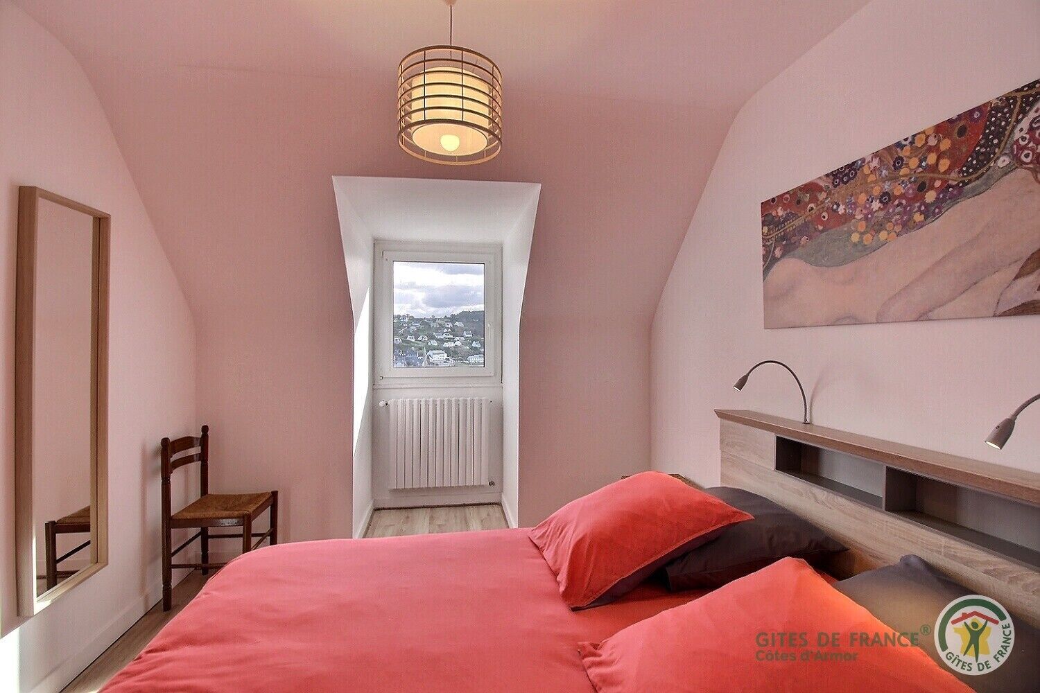Un dormitorio con una cama, una silla, un ventanal y un cuadro en la pared.