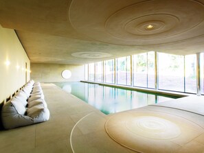 A modern indoor swimming pool with a long bench along one wall, large windows, and a unique ceiling design. - Ivy Cottage - UK42246 (Broughton, near Skipton)