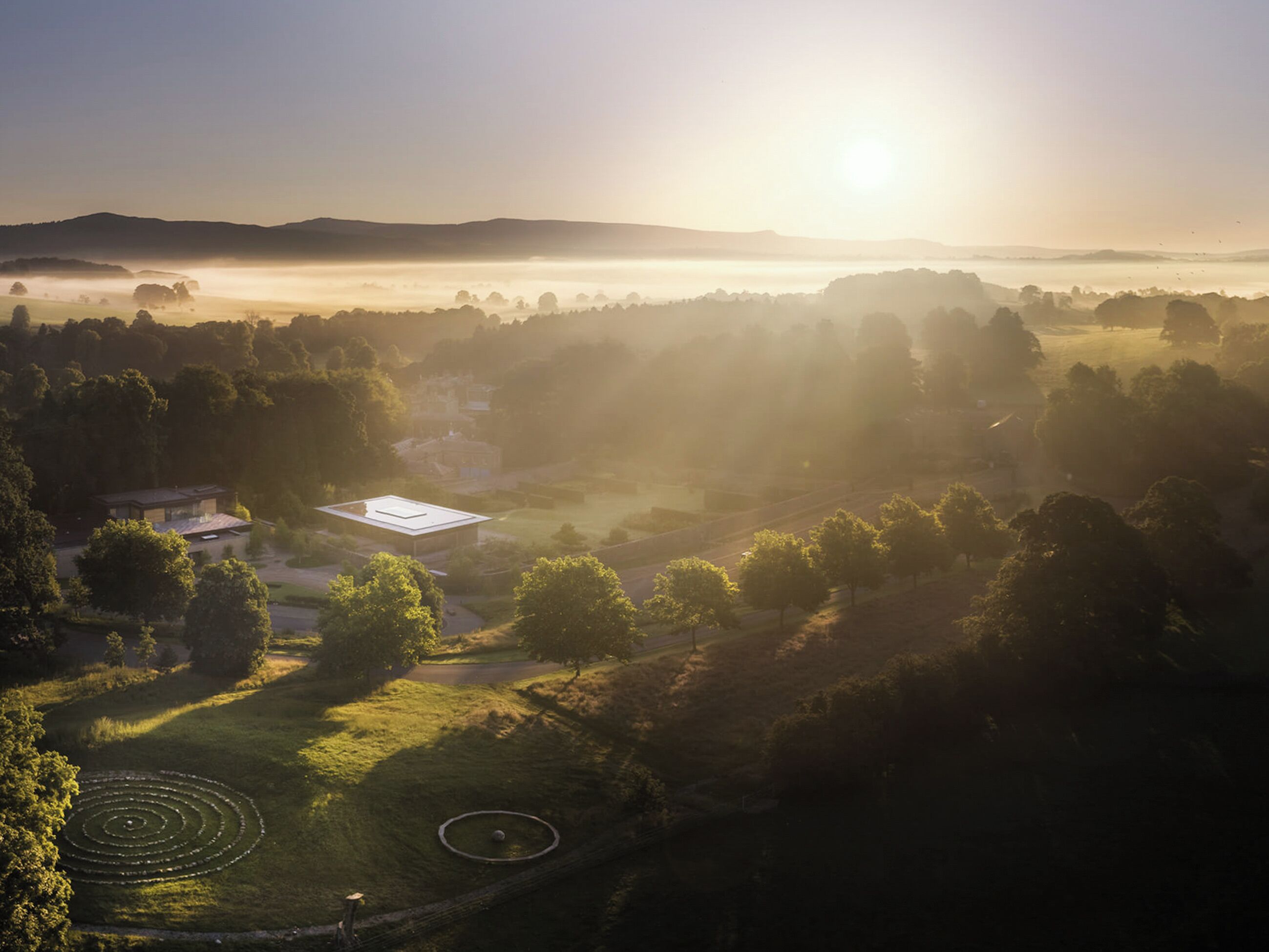 A rural landscape with a circular garden, a building with a flat roof, and a road.