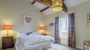 Um quarto com uma cama, duas luminárias de cabeceira, uma janela com cortinas, um radiador e uma moldura com um quadro na parede.