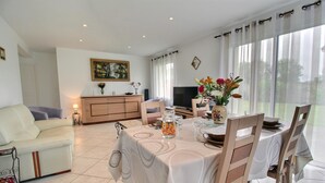 Un comedor con una mesa dispuesta para cuatro personas, un sofá, un armario y un televisor al fondo.