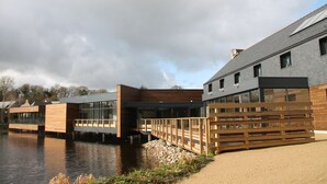 Een modern gebouw met een houten terras dat over het water uitsteekt, met grote ramen en een plat dak.