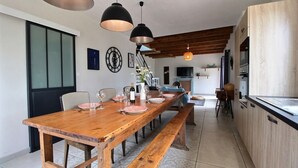 Un comedor espacioso con una larga mesa de madera, bancos e iluminación colgante.