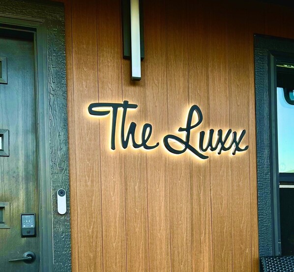 A wooden wall with a sign that reads 'The Luxx' in a cursive font.