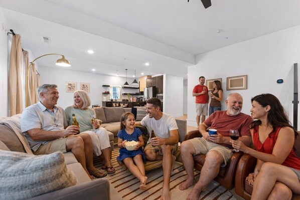 A family gathering in a modern living room with a sofa, chairs, and a dining area in the background.