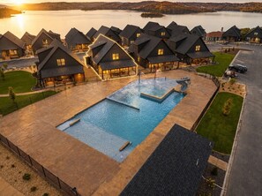 En resort med flere chalet-lignende bygninger, en central swimmingpool og udsigt til en sø i solnedgang.