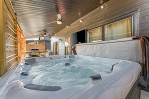 A hot tub in a wooden cabin with a ceiling fan and a view of the outside.