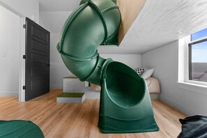 A room with a green spiral slide, a window, a door, and a bed with pillows.