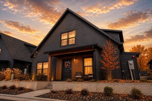 A two-story house with a dark exterior, a front porch with a bench, and a small tree.