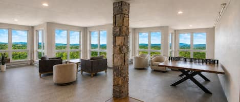 A spacious room with a ping pong table, multiple seating areas, and large windows offering a view of greenery.