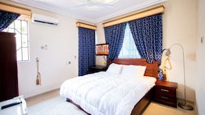 A neatly arranged bedroom with a large bed, bedside tables, a nightstand, a lamp, and a window with curtains. - Aduk Guest House (Accra)