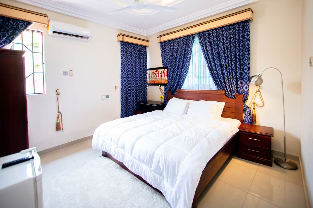A neatly arranged bedroom with a large bed, bedside tables, a nightstand, a lamp, and a window with curtains.