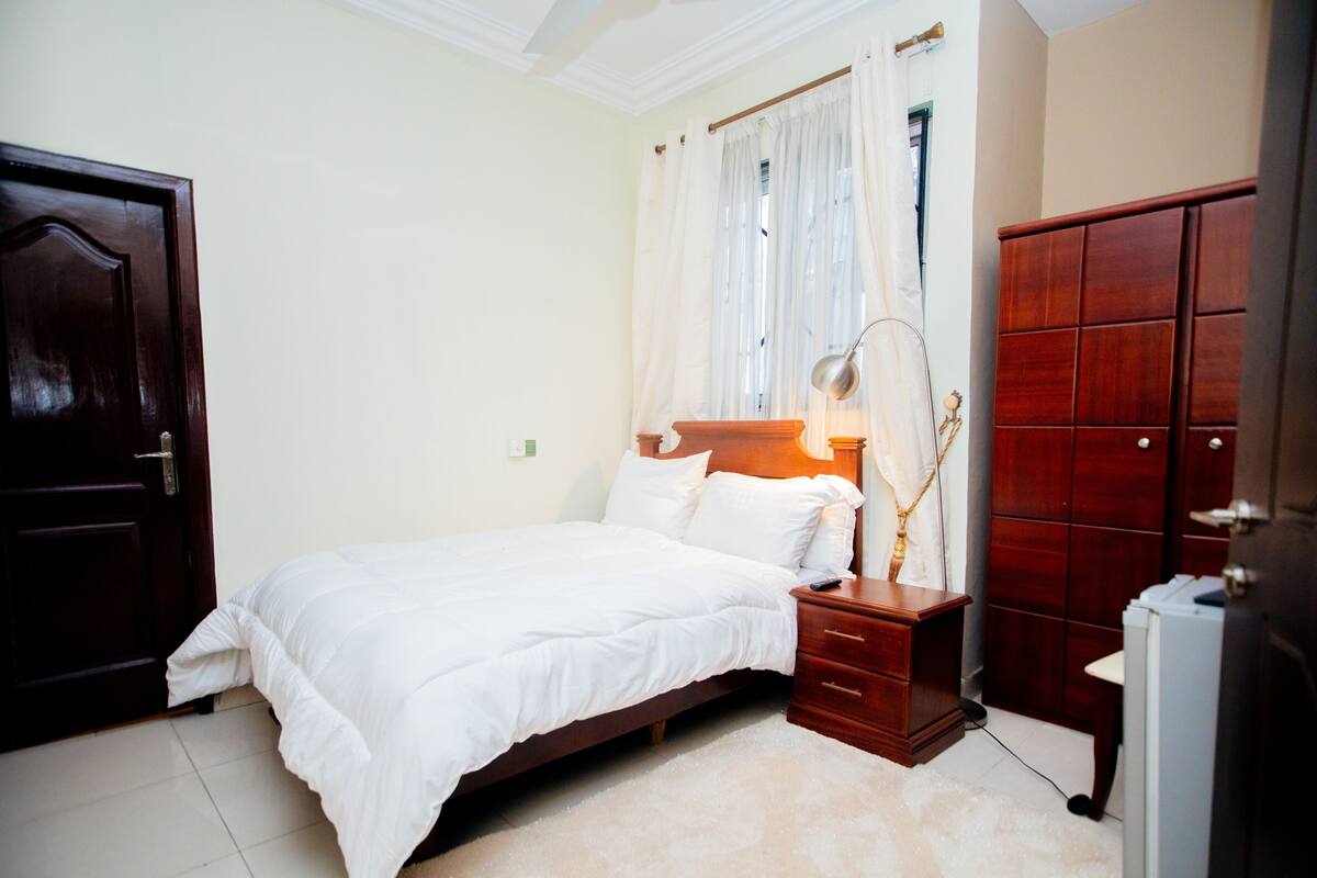 A bedroom with a bed, bedside table, lamp, wardrobe, and a door.