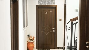 A hallway with a marble floor, a wooden door, and a potted plant. - Aduk Guest House (Accra)