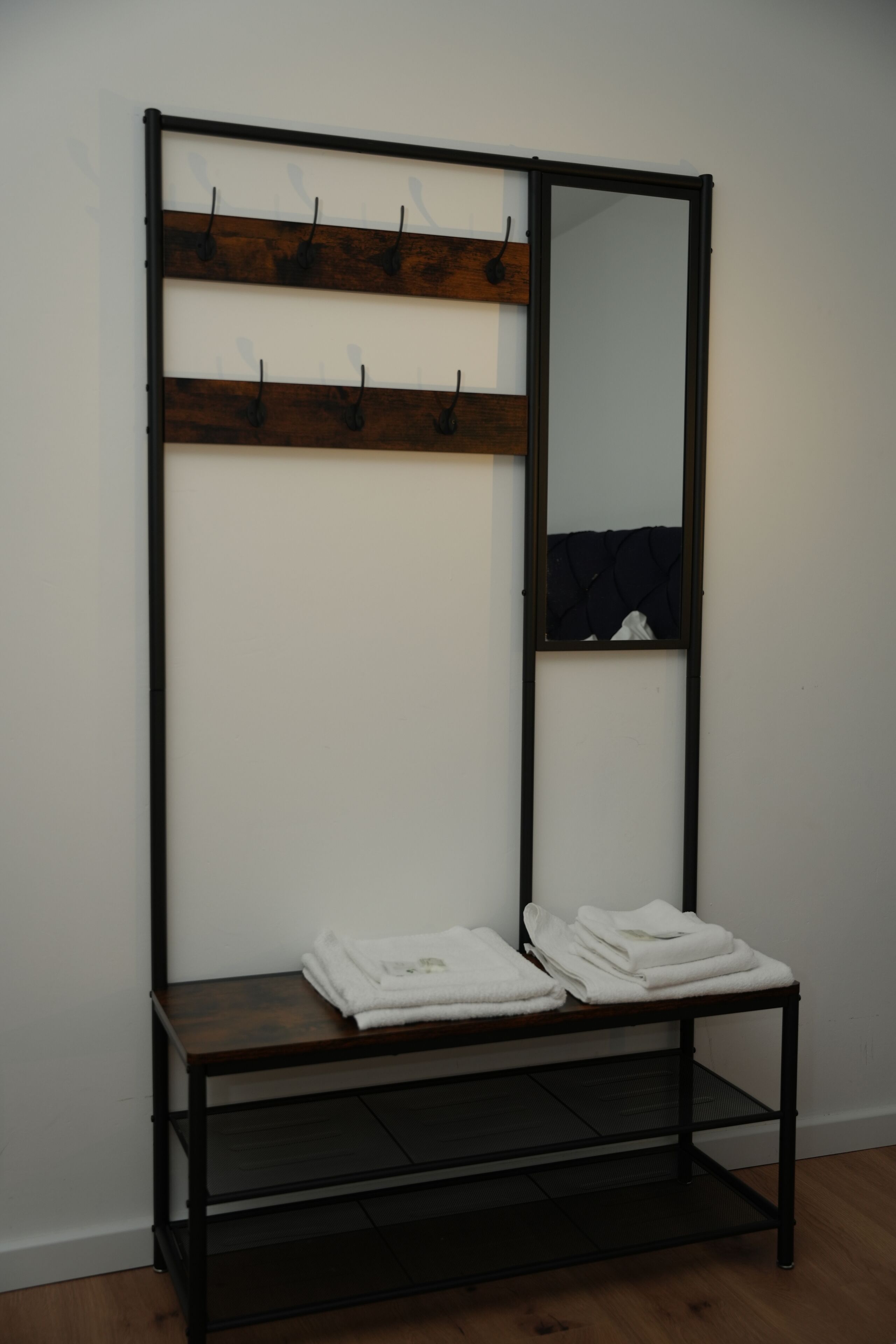 A room with a wooden coat rack, a mirror, and a shelf with folded towels.