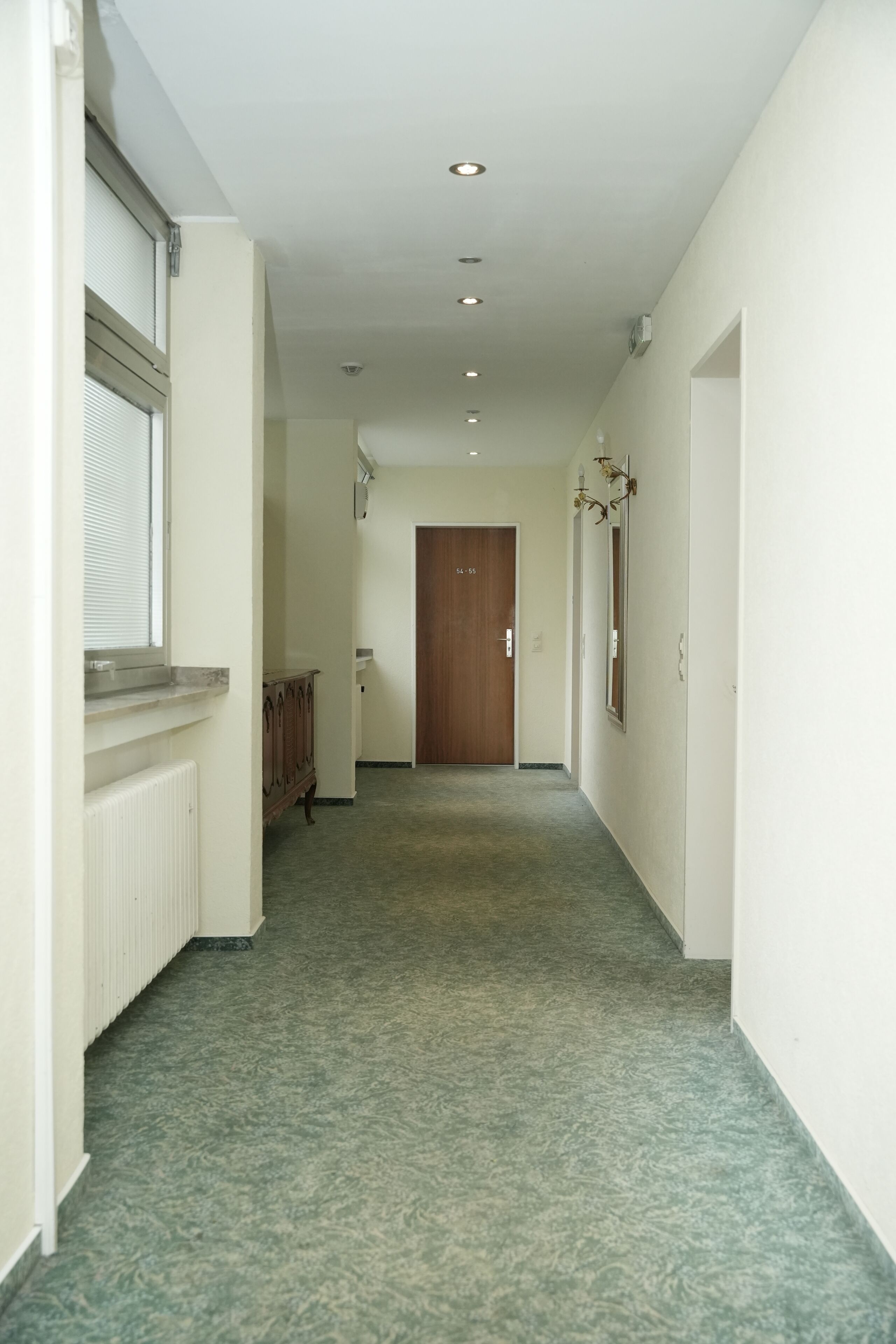A hallway with a radiator, a wooden cabinet, and a door at the end.