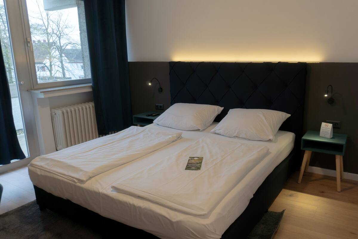 A double bed with white linens, a dark headboard, and two bedside tables with lamps.
