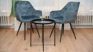 Duas cadeiras cinza com estofamento e pernas de metal preto, e uma pequena mesa redonda com um vaso de vidro em cima.