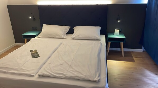 A neatly made bed with white linens, two bedside tables with lamps, and a blue curtain.