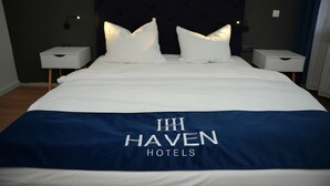Quarto de hotel com uma cama grande, duas mesas de cabeceira e cabeceira com um logotipo.