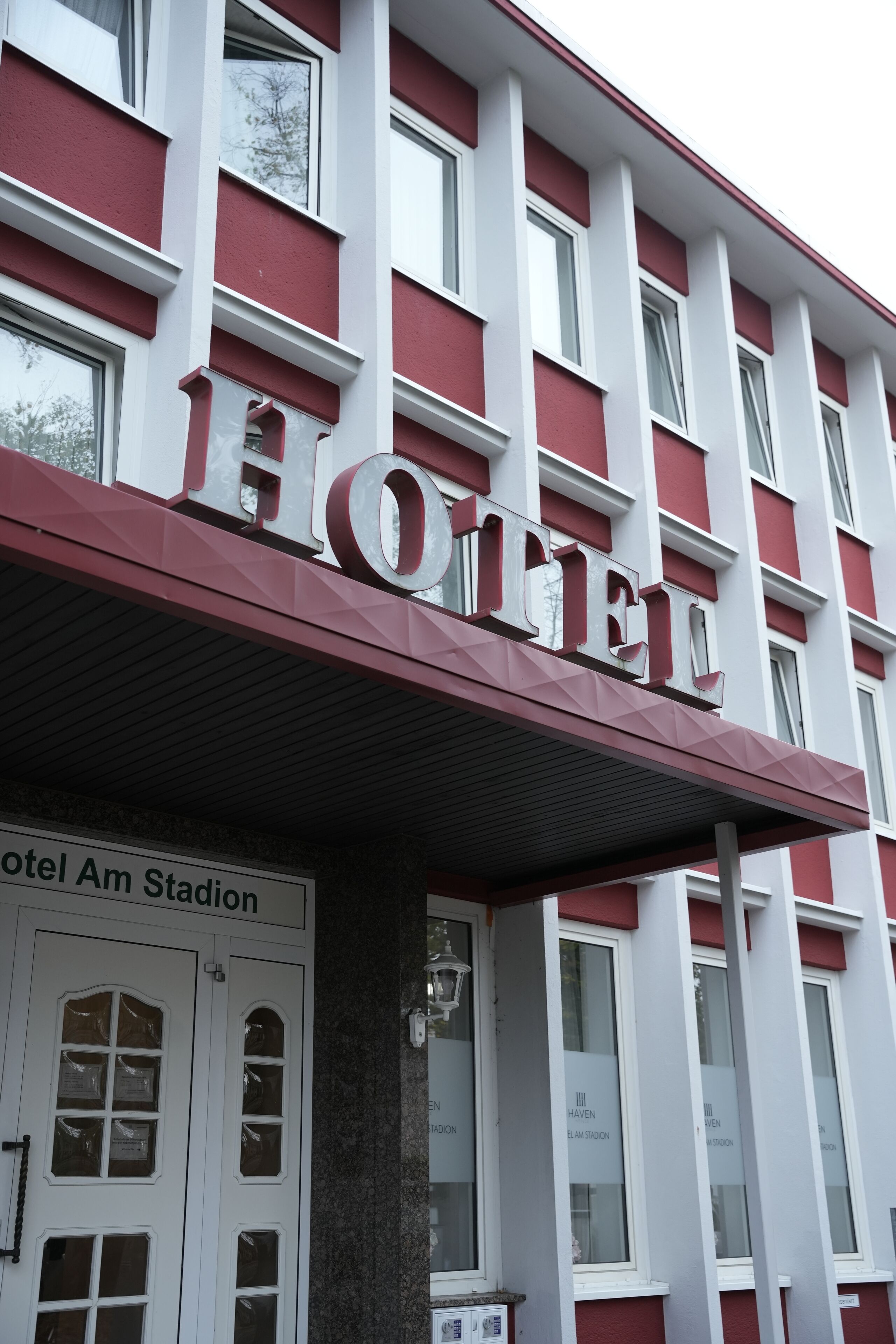 A hotel with a prominent 'HOTEL' sign, a name plaque, and a sign indicating 'Hotel Am Stadion'.