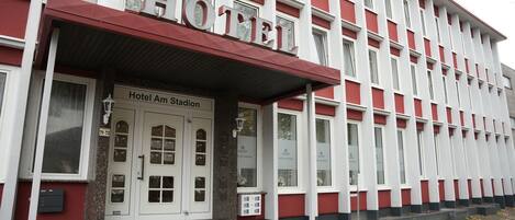 A hotel with a red and white facade, a prominent entrance with steps, and a sign reading "Hotel Am Stadion."