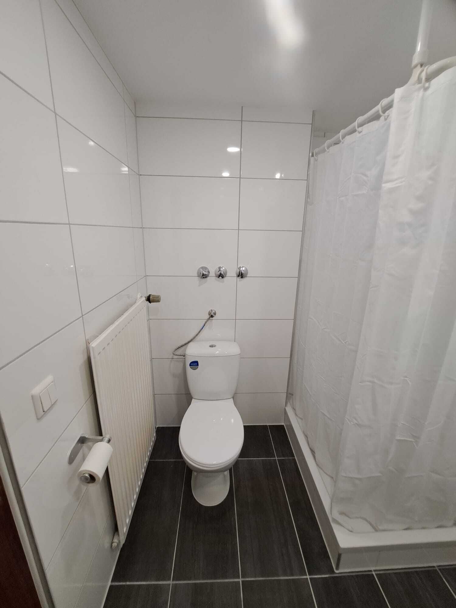 Un baño pequeño y limpio con inodoro, cortina de ducha y radiador.