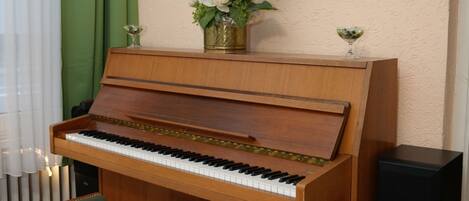 A wooden piano with a bench, a black speaker, a vase with flowers, and a framed picture on the wall.
