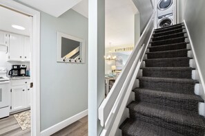 A staircase with a dark carpet and white railings leading to a laundry area with a sign that reads "BEACH HOUSE".