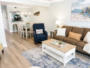A living room with a sofa, armchair, coffee table, and a dining area with chairs and a table.