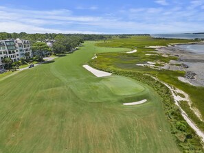 A golf course with sand bunkers, a water body, and a building complex in the background.