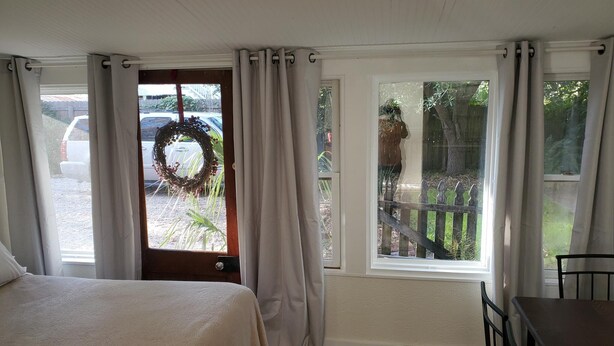 Une chambre à coucher avec un lit, une fenêtre donnant sur un jardin et une porte décorée d’une guirlande.