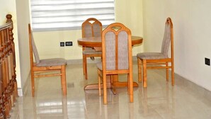 A dining area with a round table and four wooden chairs with cushioned seats. - Tamarind Guesthouse (Aburi)