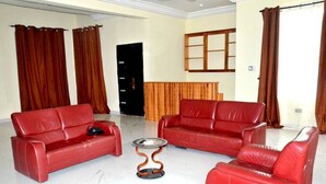 A living room with two red leather sofas, a small round table, and a wooden cabinet. - Tamarind Guesthouse (Aburi)