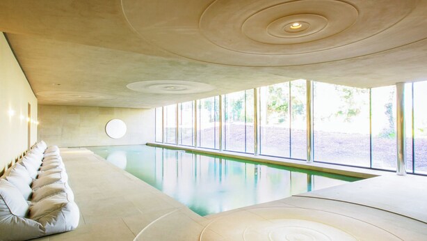 Une piscine intérieure moderne au design minimaliste, avec un long banc le long d’un des côtés et un espace de détente circulaire au centre.