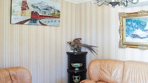 Una habitación con papel tapiz a rayas, un cuadro de un tren rojo, una escultura de pájaro y un retrato enmarcado de un paisaje nevado.