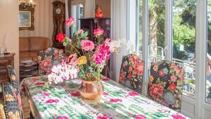 Una mesa de comedor con mantel floral, rodeada de sillas con tapicería floral, y un florero con flores.