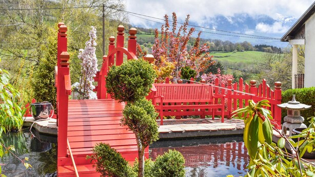 Un puente rojo sobre un estanque, con un edificio blanco al fondo.