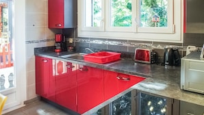 Una cocina moderna con armarios rojos, encimera negra y ventana con vistas a zonas verdes.