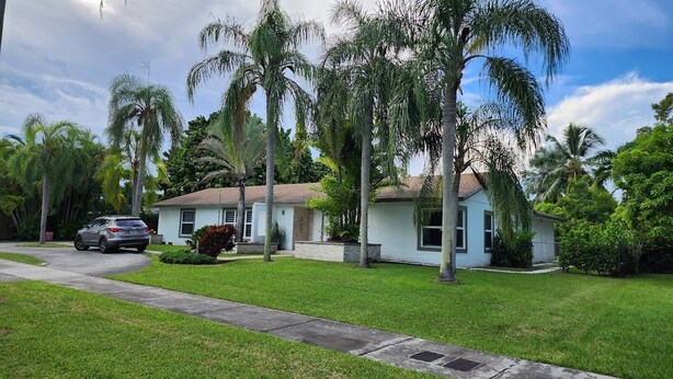 A residential house with a driveway, a parked car, and surrounding palm trees. - Private Apartment Miami Kendall near Zoo, The Falls Mall, and Miami Dade College (Miami)