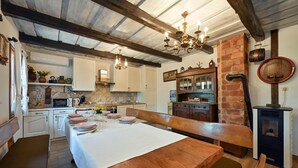 Une cuisine rustique avec une table à manger en bois, disposée pour accueillir quatre personnes, un mur en briques et un poêle d’époque.